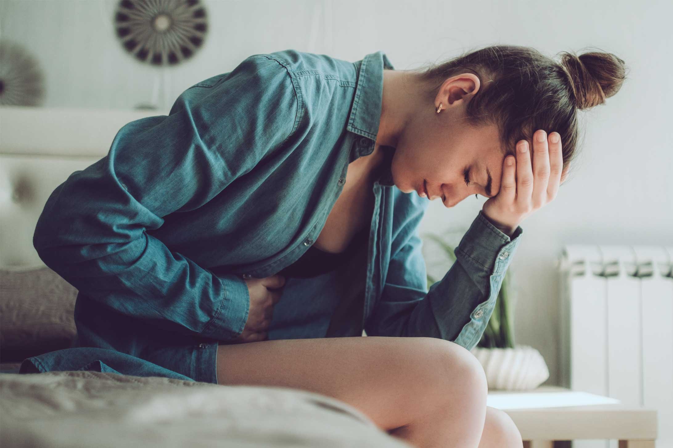 Endometriose: Eine junge Frau hält sich den Bauch und den Kopf vor Schmerz.